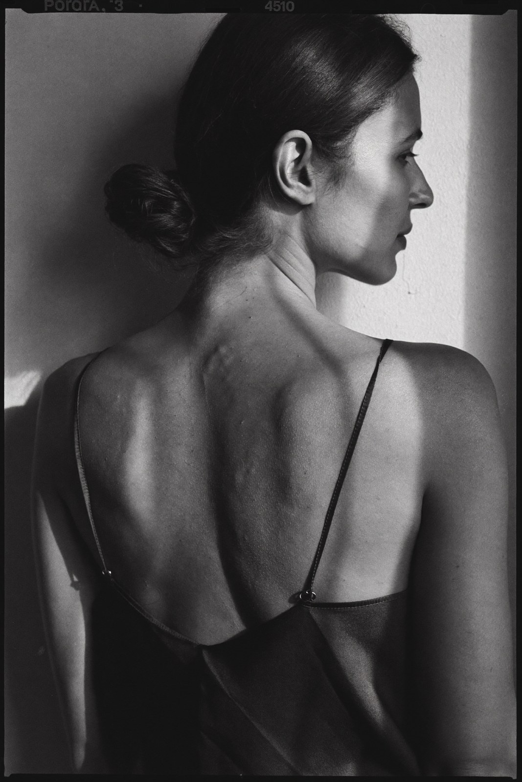 Monochrome back view in a dark silk slip, hard window light across the shoulders