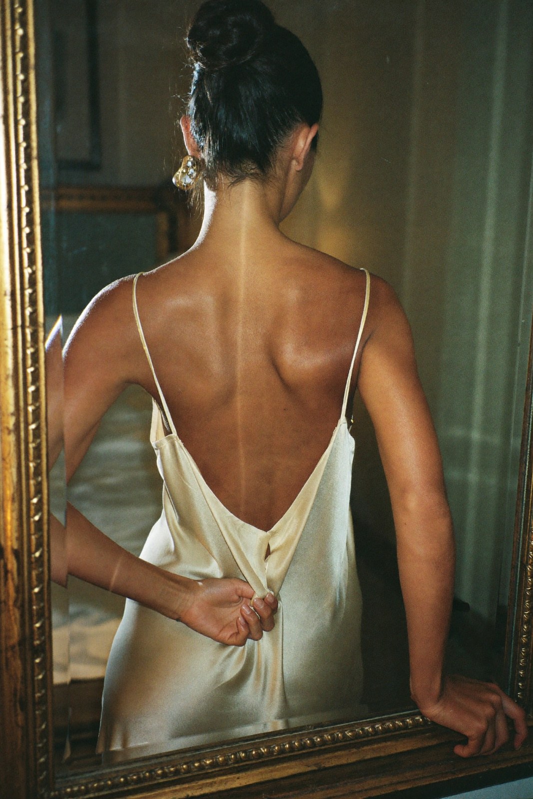 Back view and reflection in a gilt mirror, ivory silk slip, lamp light